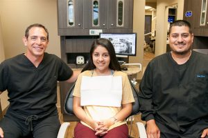 doctor and staff with patient in the dental chair and monitor behind them